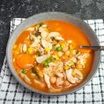 A shot of high-protein chicken noodles soup in a bowl on top of a white and green tablecloth with a black background