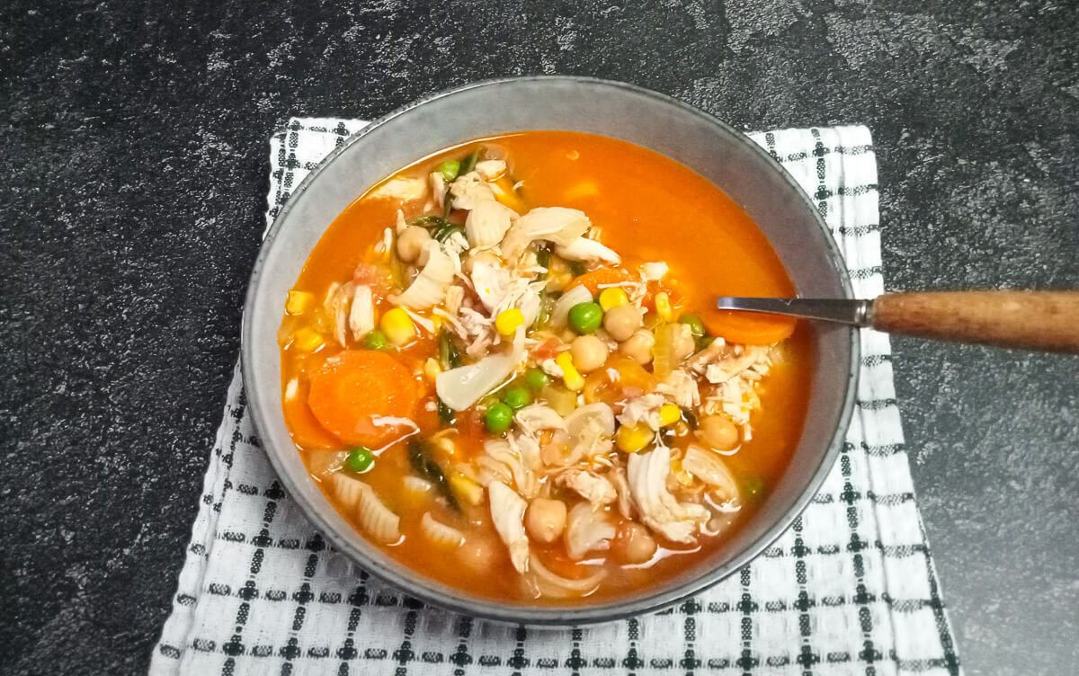 A shot of high-protein chicken noodles soup in a bowl on top of a white and green tablecloth with a black background