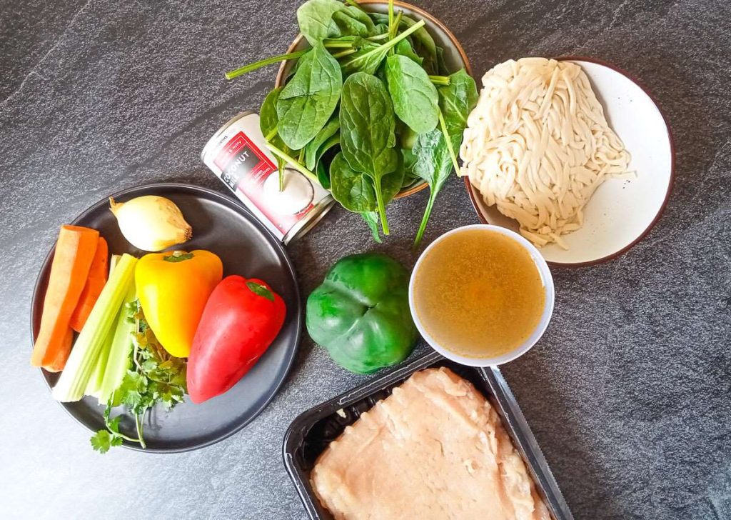 Ingredients photo: noodles, spinach, coconut milk, bell peppers, carrots, celery, onion, and ground chicken.