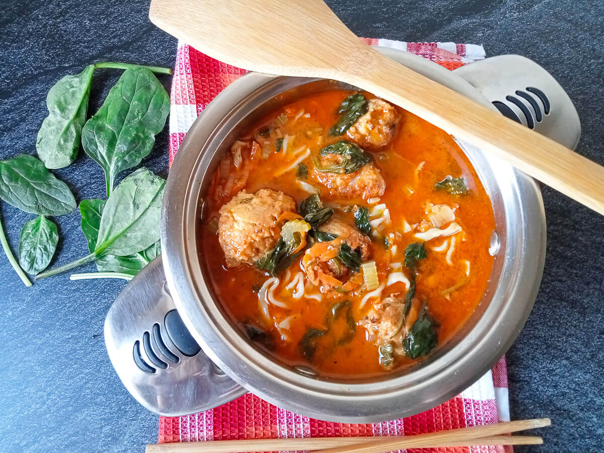 A pot of Thai chicken meatball soup with wooden spoon and chop sticks beside it.