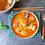 A bowl of Thai chicken meatball soup on a green tablecloth with spoon and chopstick beside it.