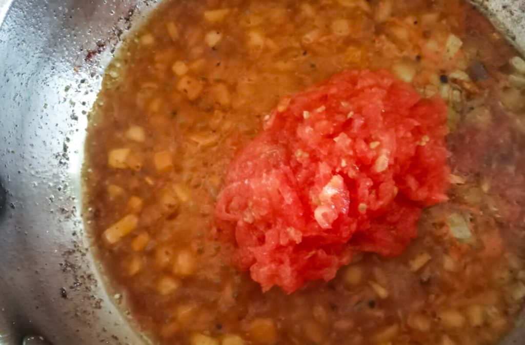 Process image: adding grated tomatoes to the pot of sauteed onions