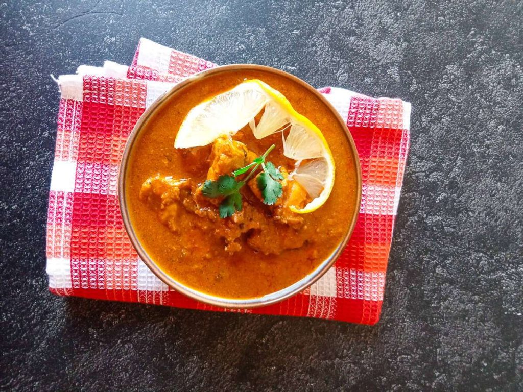 A bowl of Tikka Chicken masala soup on a tablecloth with a black background