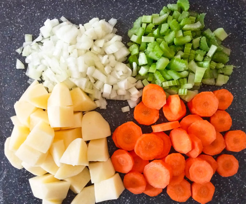 chopped onion, potatoes, celery, and carrots on a chopping board