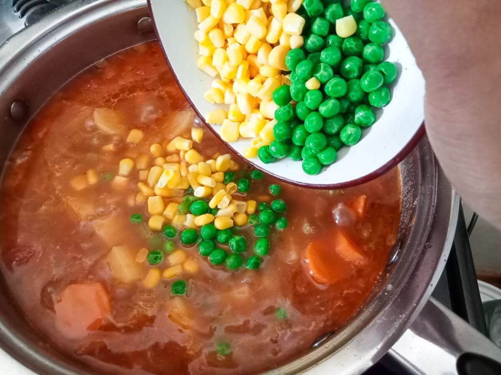 process image: adding sweet corn and peas to the pot of soup