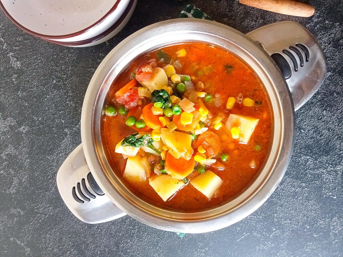 a shot of a bone broth vegetable soup pot with empty serving bowls beside it.