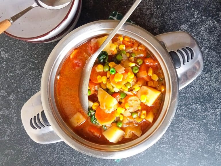 an overhead shot of a bone broth vegetable soup pot with a silver spoon in it and empty serving bowls beside it.