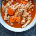 A close-up image of a bowl with chicken feet soup in it on a black background.