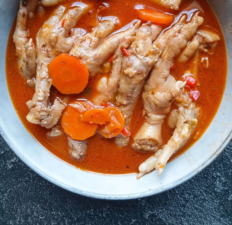 A close-up image of a bowl with chicken feet soup in it on a black background.