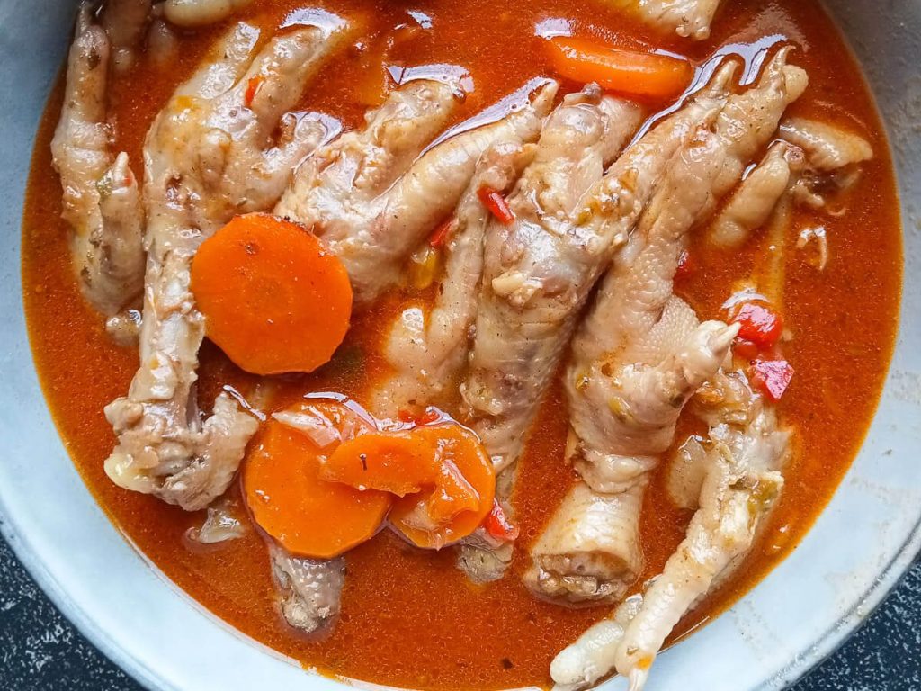 A close-up image of a bowl with chicken feet soup in it on a black background.