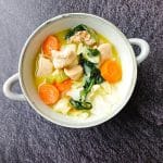 A bowl of chicken cabbage soup on a black background