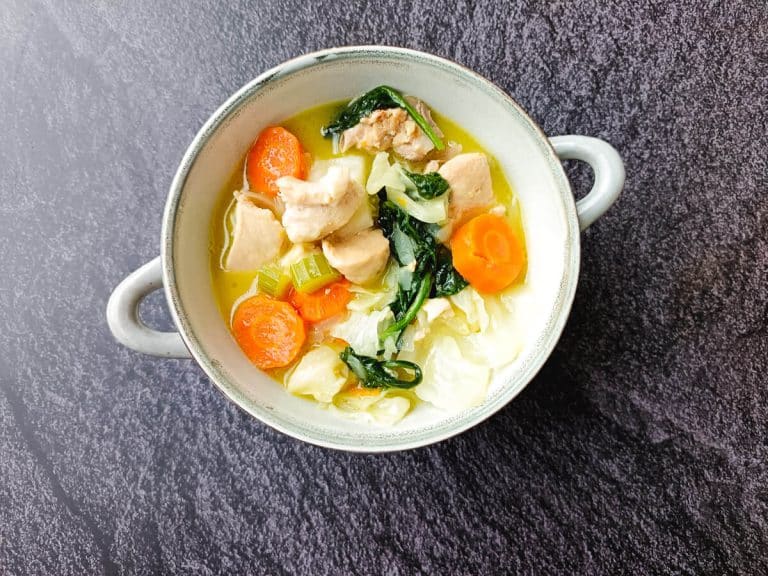 A bowl of chicken cabbage soup on a black background