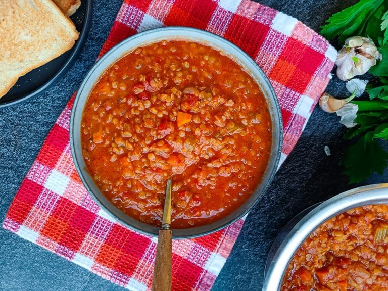 A bowl of red lentil tomato soup with a spoon in it on a tablecloth with a black background