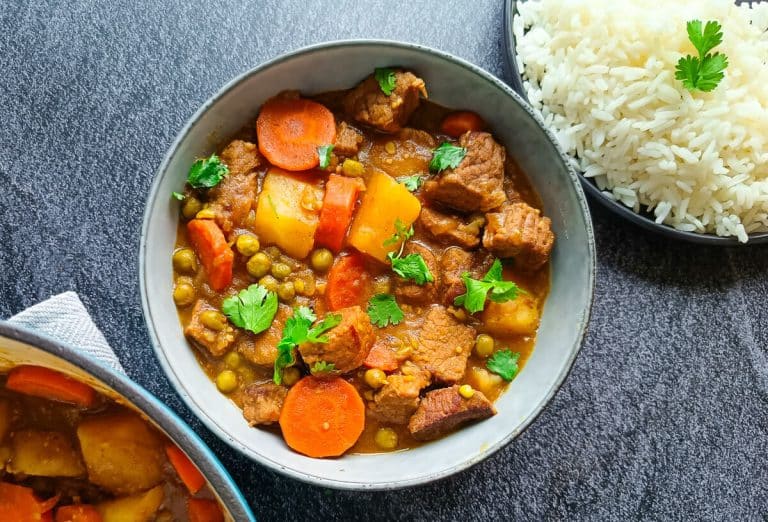 a bowl of venison stew with a plate of white rice beside it and a pot of the deer stew. The image has a black background