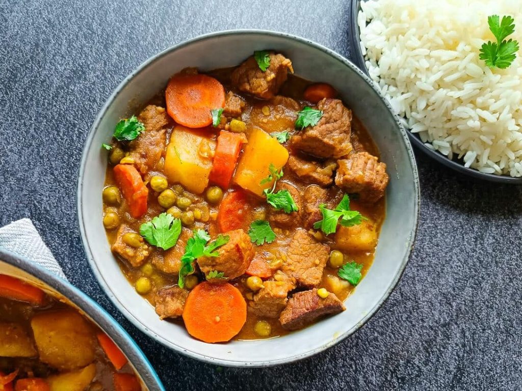 a bowl of venison stew with a plate of white rice beside it and a pot of the deer stew. The image has a black background
