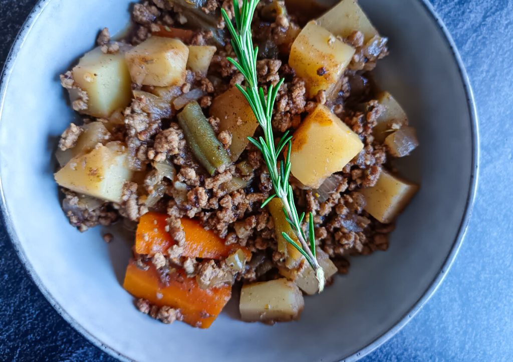An overhead shot of a hearty ground venison stew garnished with fresh thyme on a black background.