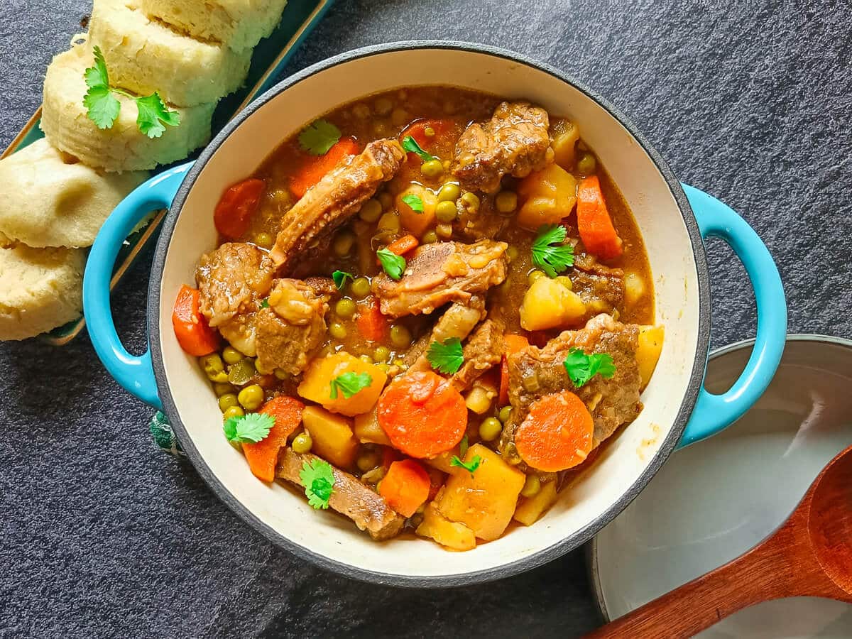 A castor iron pot of beef short rib stew with serving bowls next to it and sourdough steamed bread on a tray.