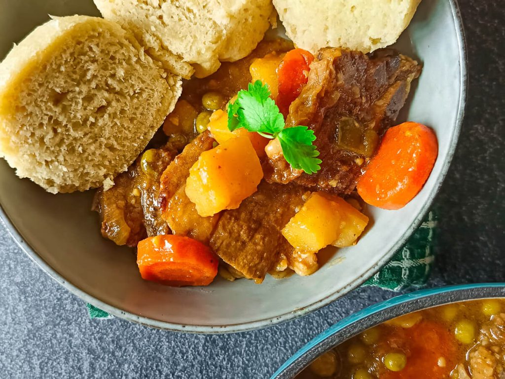 a bowl of short rib stew served with sourdough steamed bread garnished with fresh parsley leaves